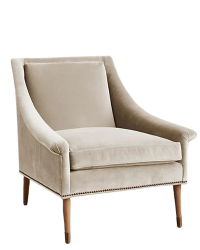 Sillón individual tapizado en beige claro, de líneas rectas con respaldo y asiento acolchados, brazos delgados y patas de madera rectas con detalle de tachas decorativas en la parte inferior.