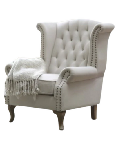 Sillón estilo clásico tapizado en color gris claro, con respaldo capitoné alto, orejas curvas, apoyabrazos redondeados y tachas decorativas, patas de madera talladas