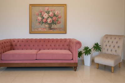Sillón Chesterfield tapizado en terciopelo rosa pastel con base y patas de madera, acompañado por una butaca capitoné en tono beige claro con patas de madera natural. Ambos muebles se encuentran en un ambiente minimalista con piso de mármol claro y una planta decorativa en maceta blanca.