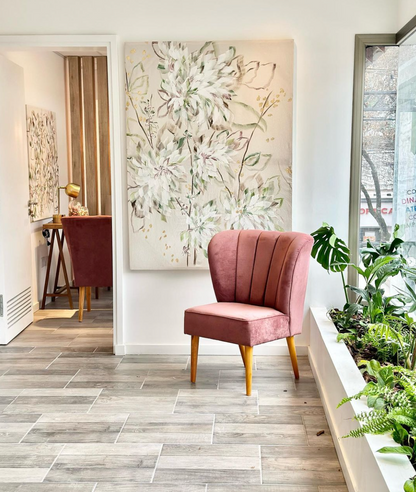 Sillón rosa junto a una ventana, con un cuadro floral detrás de un vidrio en el fondo