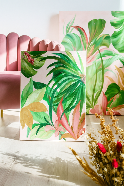 Dos cuadros de estilo tropical con hojas verdes y detalles rosados apoyados en la pared, al lado de un sillón rosa.