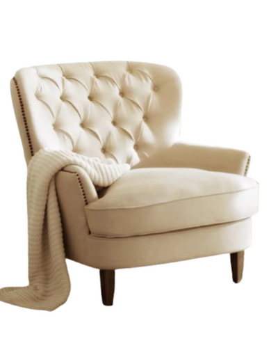 Sillón clásico tapizado en color crema con respaldo capitoné curvo, asiento acolchado y patas de madera cónicas.