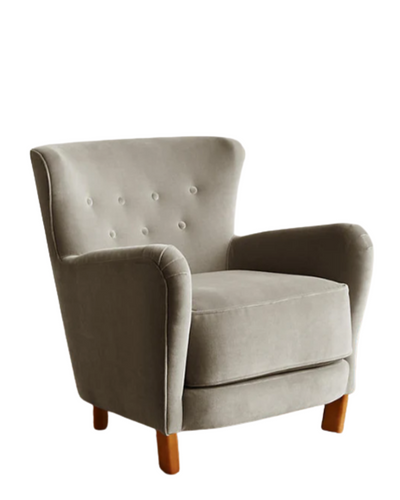 Sillón individual tapizado en gris claro, con respaldo suavemente inclinado y capitoné de botones, brazos redondeados y patas cortas de madera.