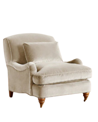 Sillón individual tapizado en beige claro, con cojín lumbar suelto, apoyabrazos curvos, respaldo levemente inclinado y patas torneadas de madera en tono medio.