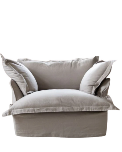 Sillón individual tapizado en lino beige claro, de estilo desenfundable, con asiento y respaldo mullidos, acompañado por dos cojines laterales sueltos que aportan volumen y comodidad.
