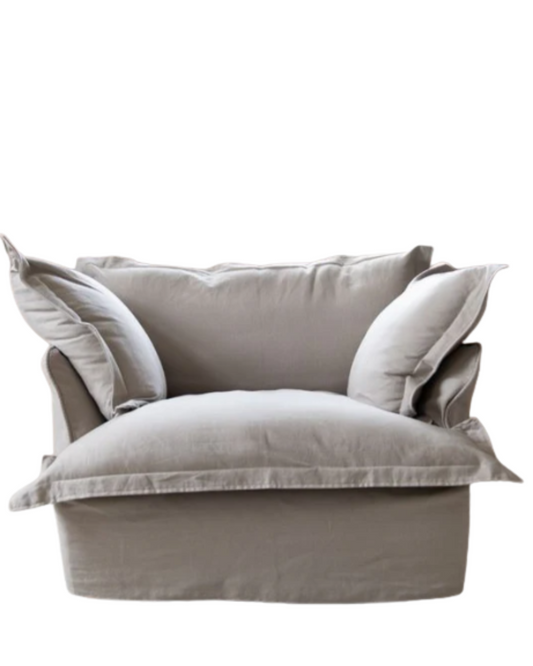 Sillón individual tapizado en lino beige claro, de estilo desenfundable, con asiento y respaldo mullidos, acompañado por dos cojines laterales sueltos que aportan volumen y comodidad.