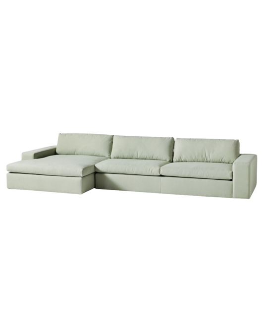Sillón esquinero tapizado en gris, diseño lineal con base baja y almohadones grandes. Estética minimalista y fresca.