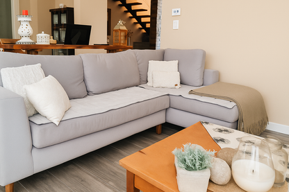 Un sillón de dos cuerpos en color gris claro, de diseño moderno y líneas rectas, se ubica en una sala iluminada por luz natural. Está decorado con cojines en tonos neutros, aportando comodidad y un estilo acogedor al ambiente