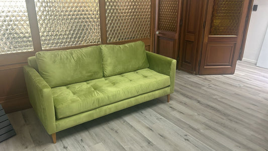 Sofá de tres cuerpos en tono verde, con diseño moderno y patas de madera, colocado en un ambiente interior con piso de madera clara.