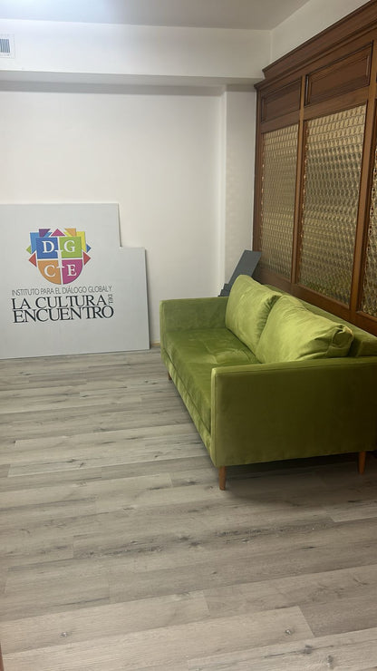 Sofá de tres cuerpos en tono verde, con diseño moderno y patas de madera, colocado en un ambiente interior con piso de madera clara.