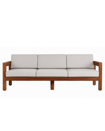Fotografía editorial de un living elegante con un gran ventanal abierto hacia un patio con plantas. En el interior, destaca un sillón de tres cuerpos con estructura de madera noble y almohadones gris claro, acompañado por una mesa ratona redonda, una alfombra con texturas y un sillón individual de cuero.
