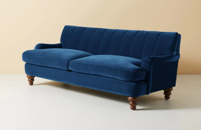 Vista completa del sofá modelo Malaika tapizado con respaldo vainillado profundo, brazos curvos y elegantes patas de madera oscura torneada, ubicado sobre fondo blanco, ideal para salas de estar, livings modernos o espacios clásicos que buscan un mueble llamativo y sofisticado.