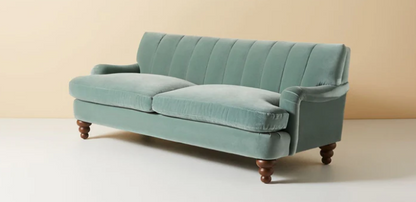 Vista completa del sofá modelo Malaika tapizado con respaldo vainillado profundo, brazos curvos y elegantes patas de madera oscura torneada, ubicado sobre fondo blanco, ideal para salas de estar, livings modernos o espacios clásicos que buscan un mueble llamativo y sofisticado.