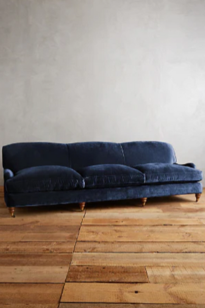 Sofá moderno modelo Minerva, tapizado con respaldo bajo y cojines de gran tamaño, estructura de líneas limpias y patas de madera clara, sobre fondo blanco, perfecto para ambientes minimalistas o espacios amplios y contemporáneos que buscan un toque de sofisticación.