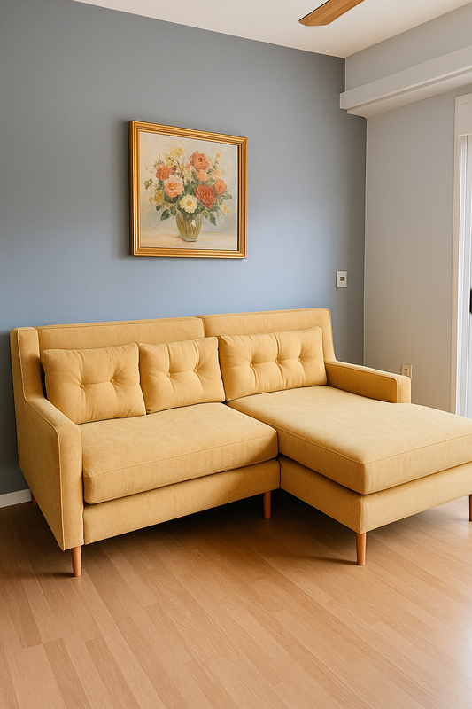 Sofá esquinero de dos cuerpos con chaise longue, tapizado en color mostaza con respaldo y asiento capitoné. Su diseño moderno y patas de madera clara destacan sobre el piso de parquet, aportando calidez y estilo contemporáneo al ambiente