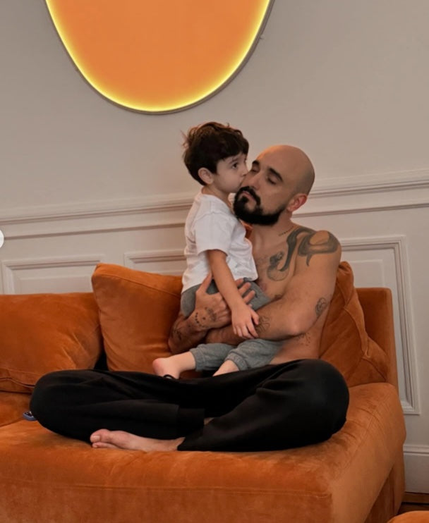 Abel Pintos sentado en su Sofá Elton color ladrillo, con un niño que le da un beso, en el living de su casa en Recoleta