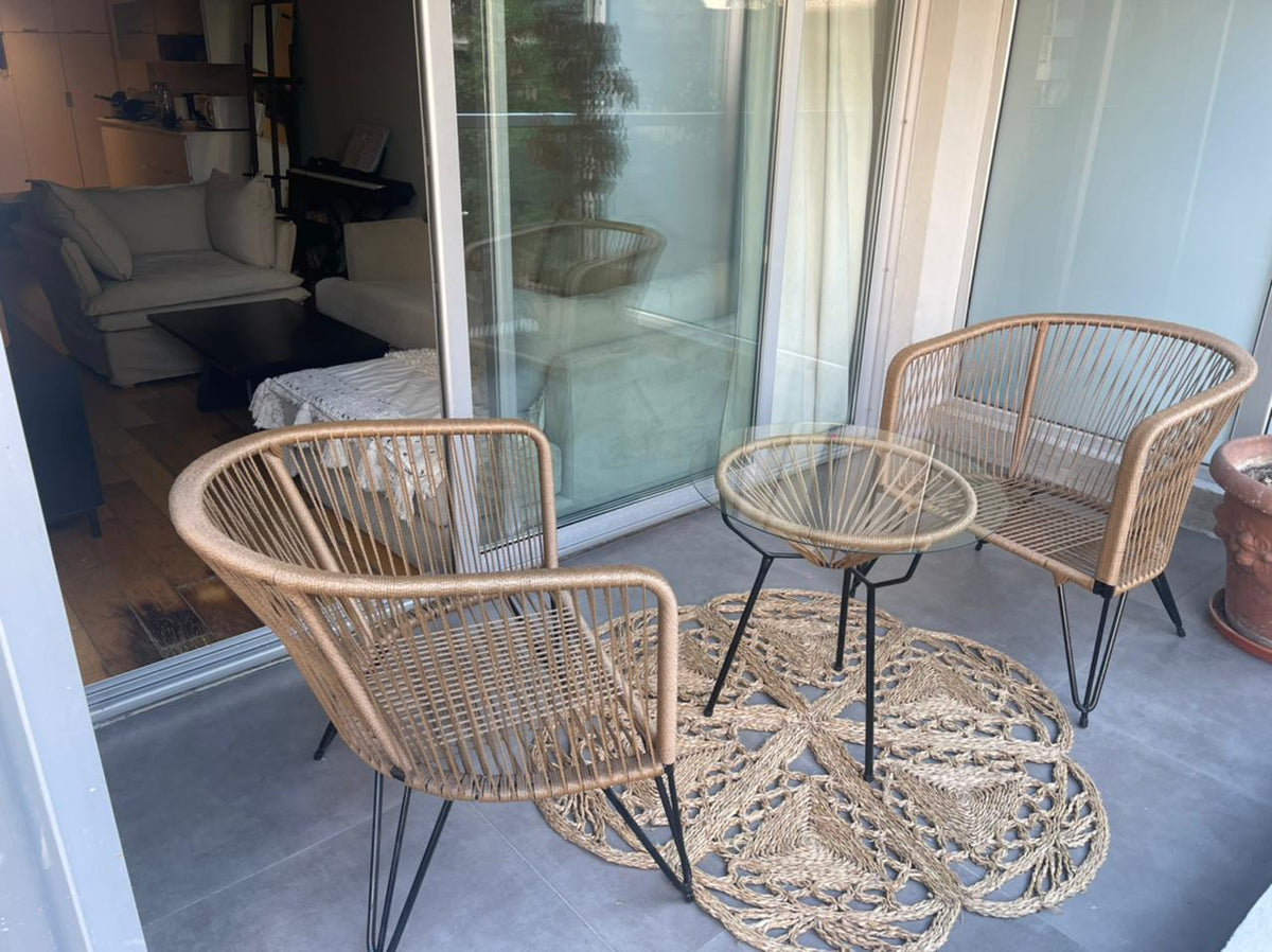 Balcón del departamento de Valen en Palacio Bellini, con dos sillas de fibra natural y mesa de vidrio