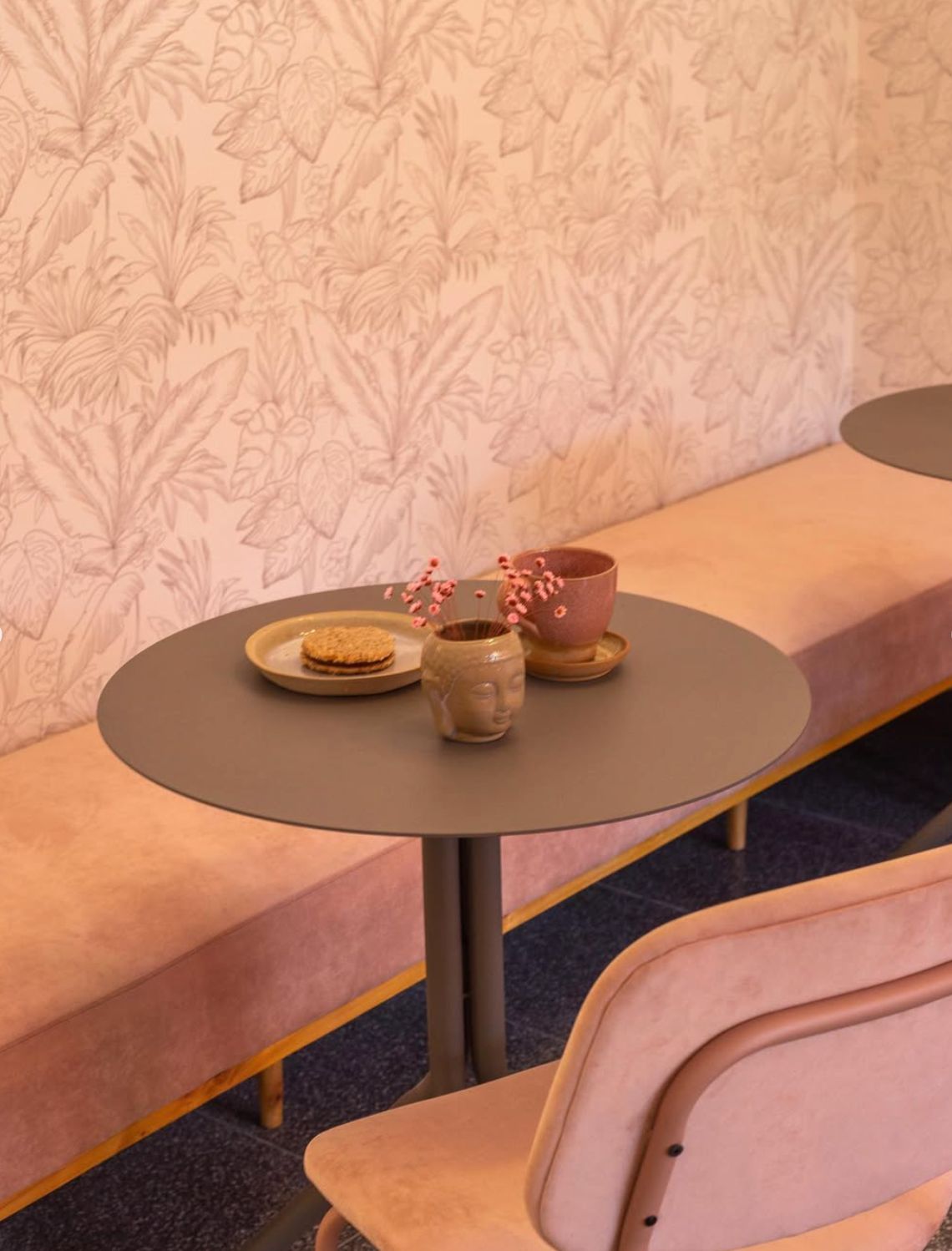 Banco corrido tapizado en rosa empolvado junto a una mesa redonda y una silla rosa en Paraíso Deli