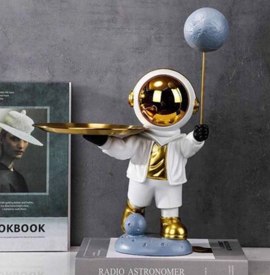 Astronauta de traje blanco y visor dorado sobre base de luna, con globo planeta y bandeja dorada