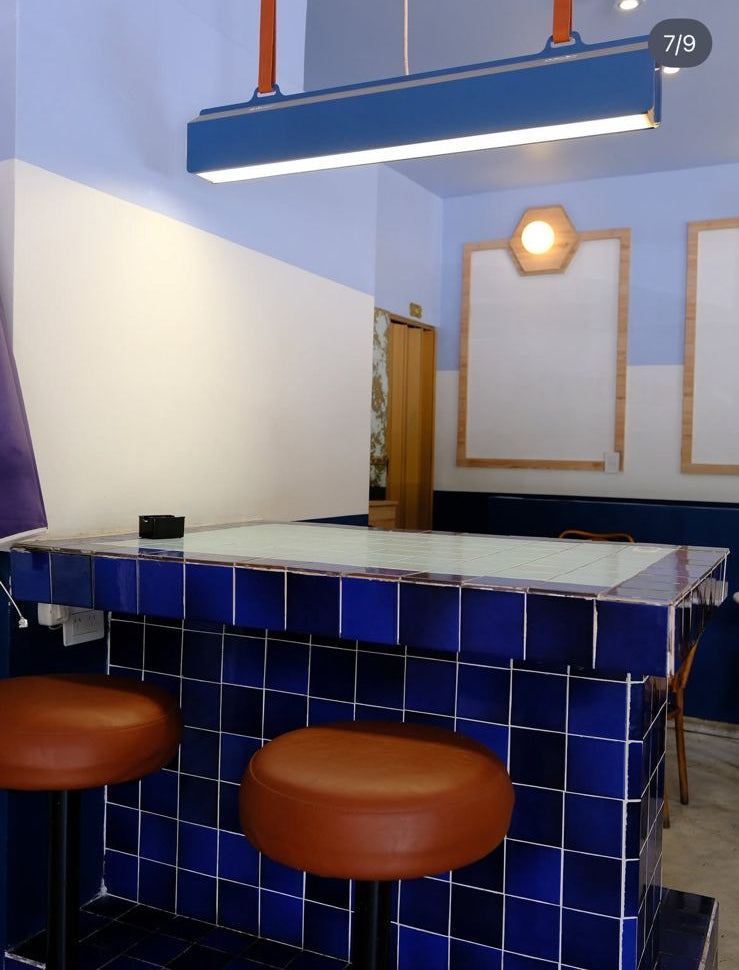 Banquetas de barra redondas tapizadas en tono suela frente a la barra de azulejos azules de Café Polvorín