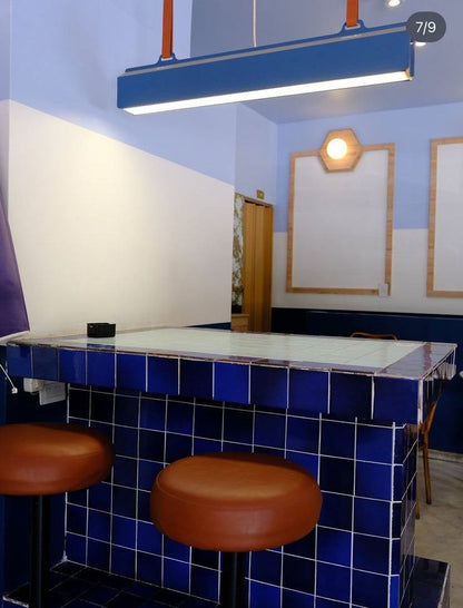 Banquetas de barra redondas tapizadas en tono suela frente a la barra de azulejos azules de Café Polvorín