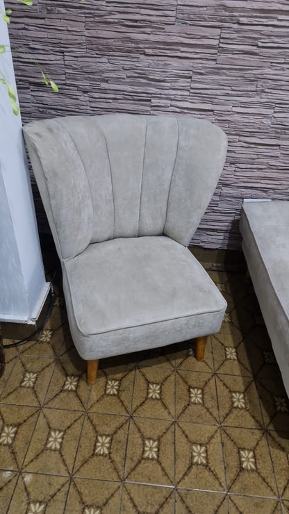 Butaca Tita gris con respaldo en abanico con canales y patas de madera, junto a la pared de piedra del living de Rocío