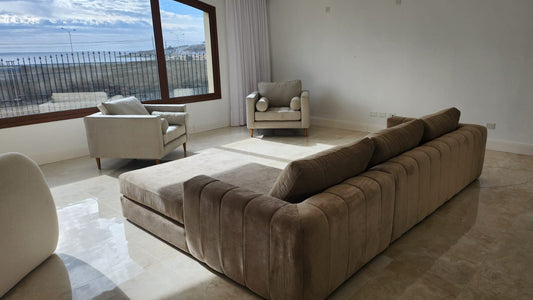 Living de la casa de Dani en Puerto Madryn con el sofá esquinero a medida de respaldo acanalado y Sillones Bambú frente a los ventanales con vista al mar