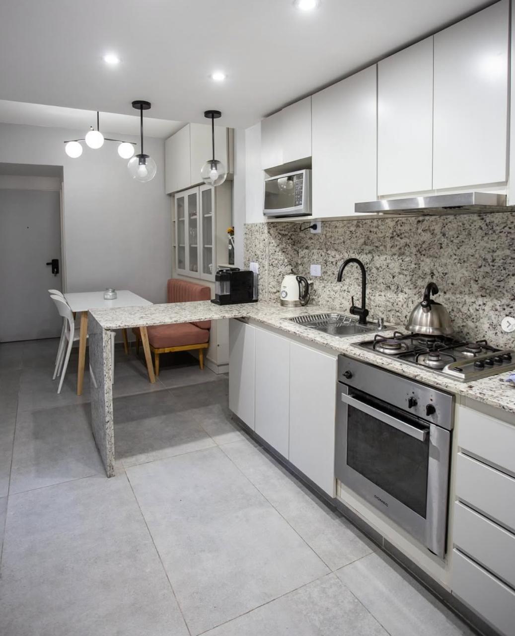 Cocina integrada con muebles blancos y mesada de granito, con el banco terracota a medida al fondo, junto a WN Interiores