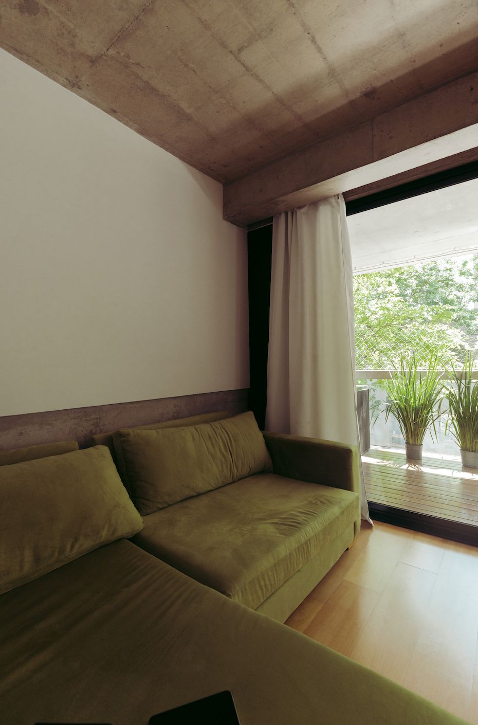 Detalle de los almohadones del Sillón Esquinero Richard verde junto al ventanal del loft