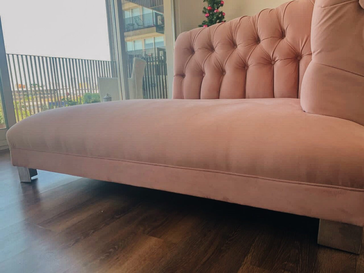 Vista baja del diván rosa de terciopelo con patas metálicas, junto al ventanal del departamento de Melisa en Retiro