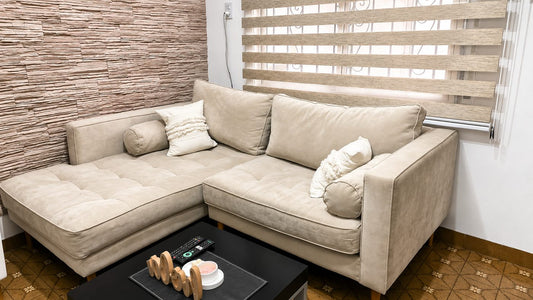 Esquinero Bambú beige claro con asiento capitoné y almohadones cilíndricos, junto a la pared de piedra del living de Rocío