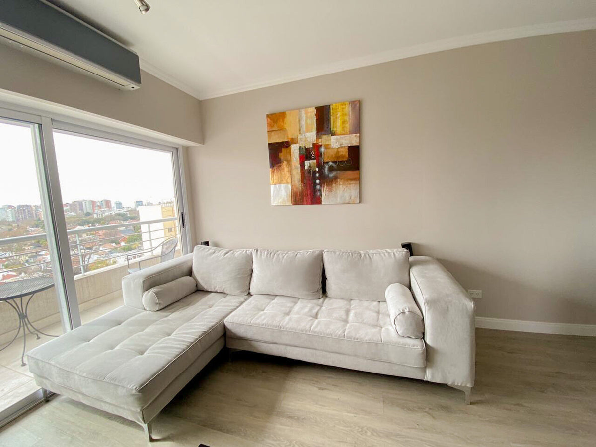 Esquinero Bambú gris perla con asiento capitoné, rolos y chaise longue junto al ventanal, en el living de Milena con vista a la ciudad
