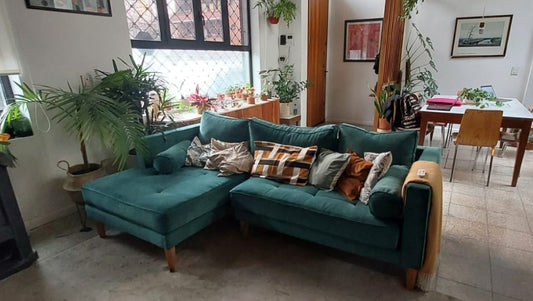 Esquinero Bambú de terciopelo verde con almohadones estampados y patas de madera, en un living con plantas junto al comedor
