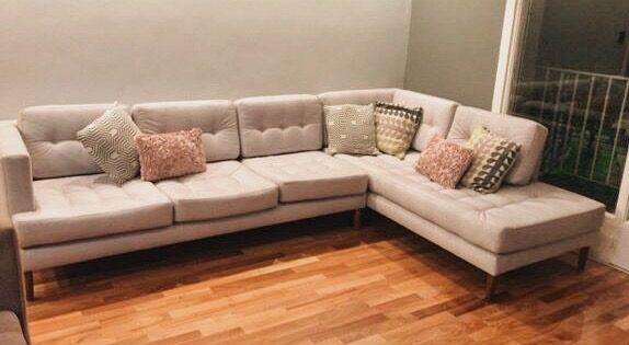Vista frontal del esquinero beige capitoné de Silvia, con almohadones decorativos rosa y estampados