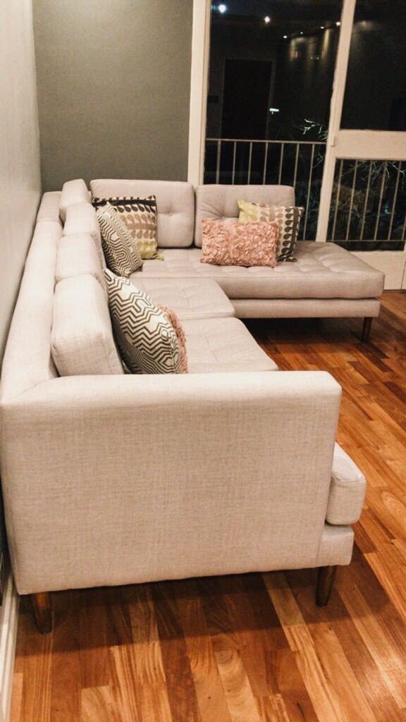 Esquinero en L beige a medida, con asiento capitoné y almohadones de respaldo con botones, junto al balcón del living de Silvia