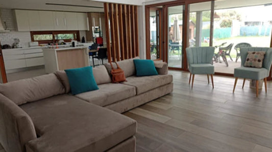 Esquinero en L a medida en pana beige con almohadones turquesa y dos Sillones Matero Tita verde agua junto al ventanal, en un living de City Bell