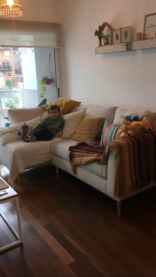 Sillón Esquinero Bélgica beige con patas de madera en el living con balcón de Antonella, con almohadones mostaza y una manta tejida