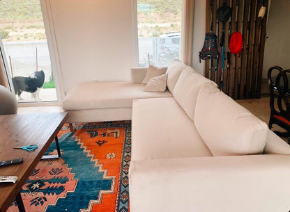 Esquinero Bélgica blanco en el living de campo de Mariana, con alfombra kilim naranja y el border collie de la familia en el ventanal