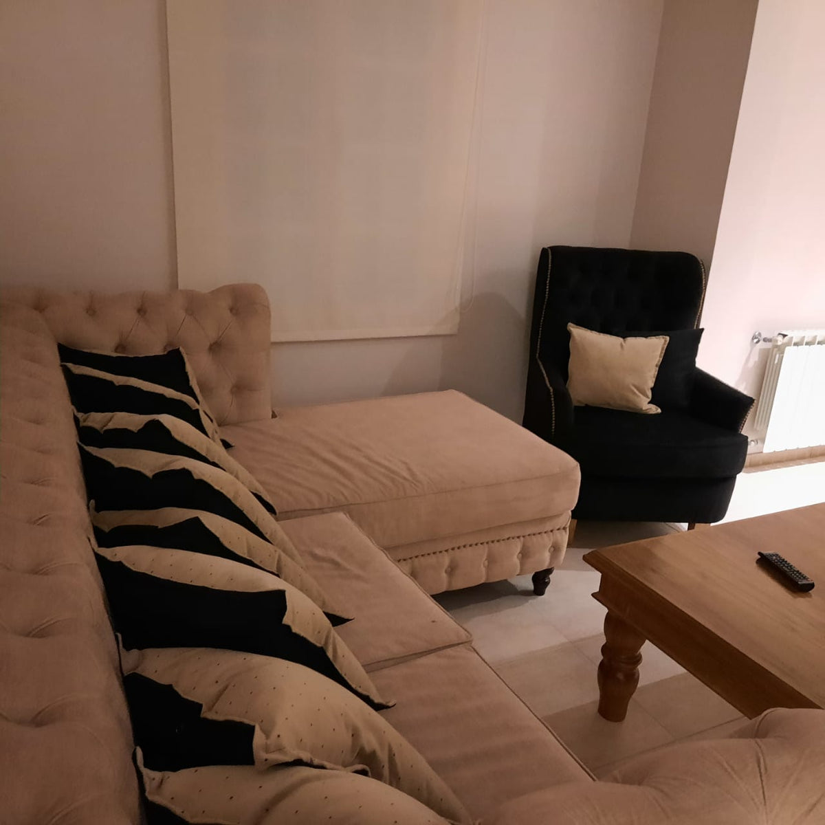 Esquinero Chesterfield beige con almohadones negros y mesa rústica de madera, en el living de Rocío