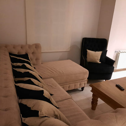 Esquinero Chesterfield beige con almohadones negros y mesa rústica de madera, en el living de Rocío