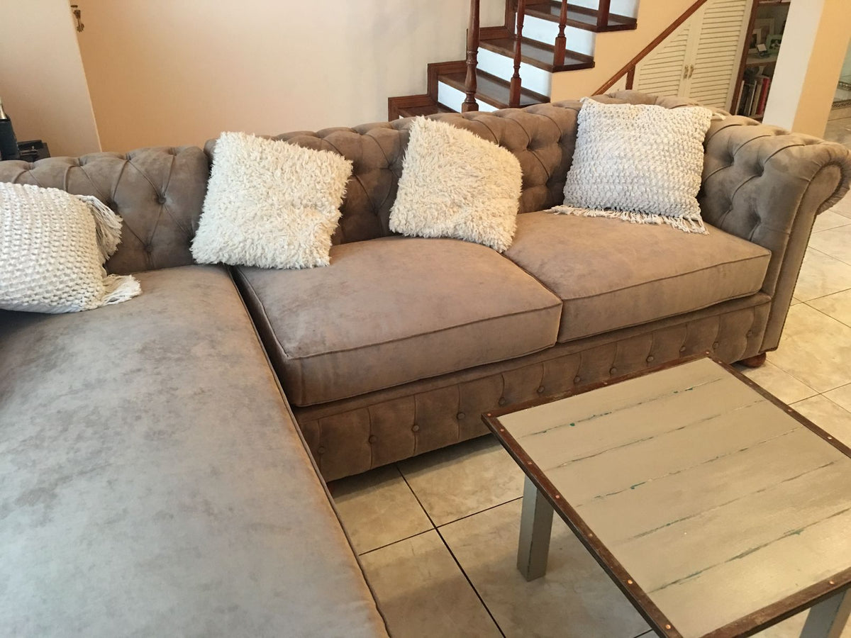 Esquinero Chesterfield beige con capitoné y brazo enrollado, frente a la escalera de madera del living de Micaela