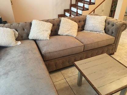 Esquinero Chesterfield beige con capitoné y brazo enrollado, frente a la escalera de madera del living de Micaela