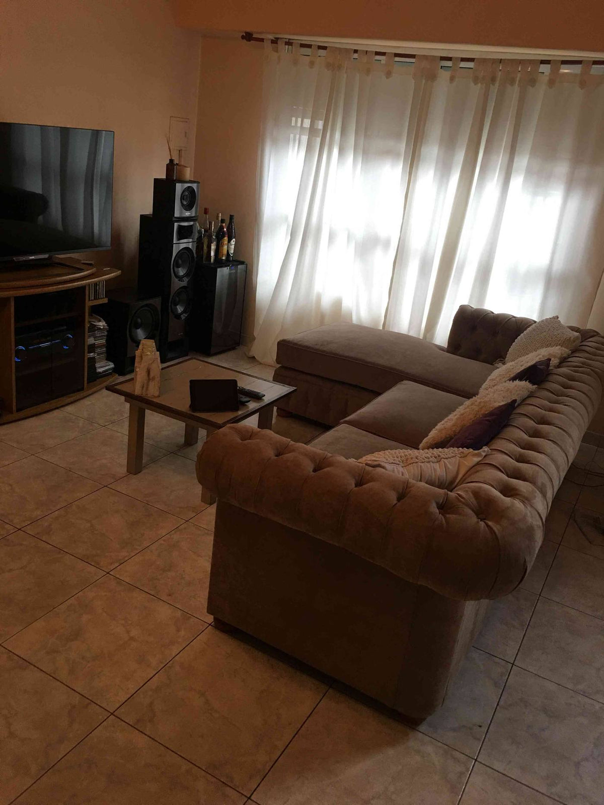 Living de Micaela con el Esquinero Chesterfield beige frente al televisor y los ventanales con cortinas claras