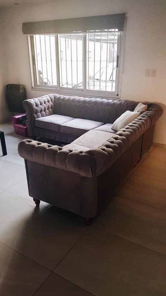 Esquinero Chesterfield gris en L, con capitoné, brazos enrollados y patas torneadas, en el living de Carla en Morón