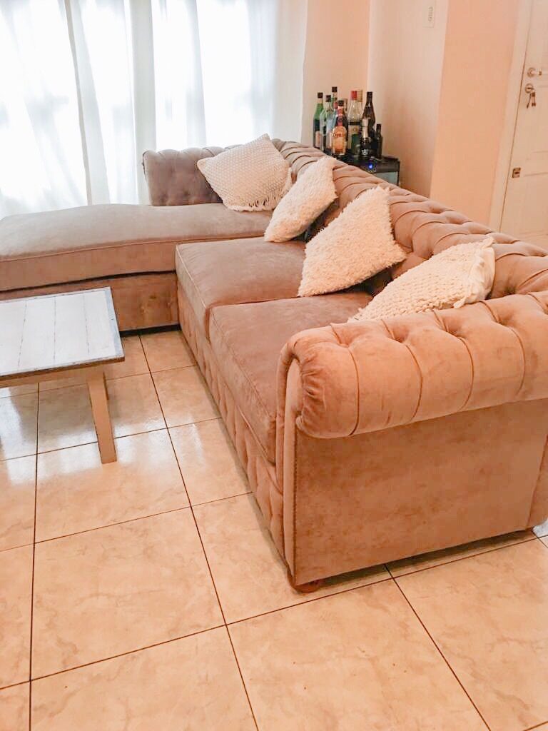 Esquinero Chesterfield rosa con chaise longue y almohadones tejidos en un living luminoso