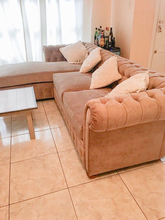 Esquinero Chesterfield rosa con chaise longue y almohadones tejidos en un living luminoso