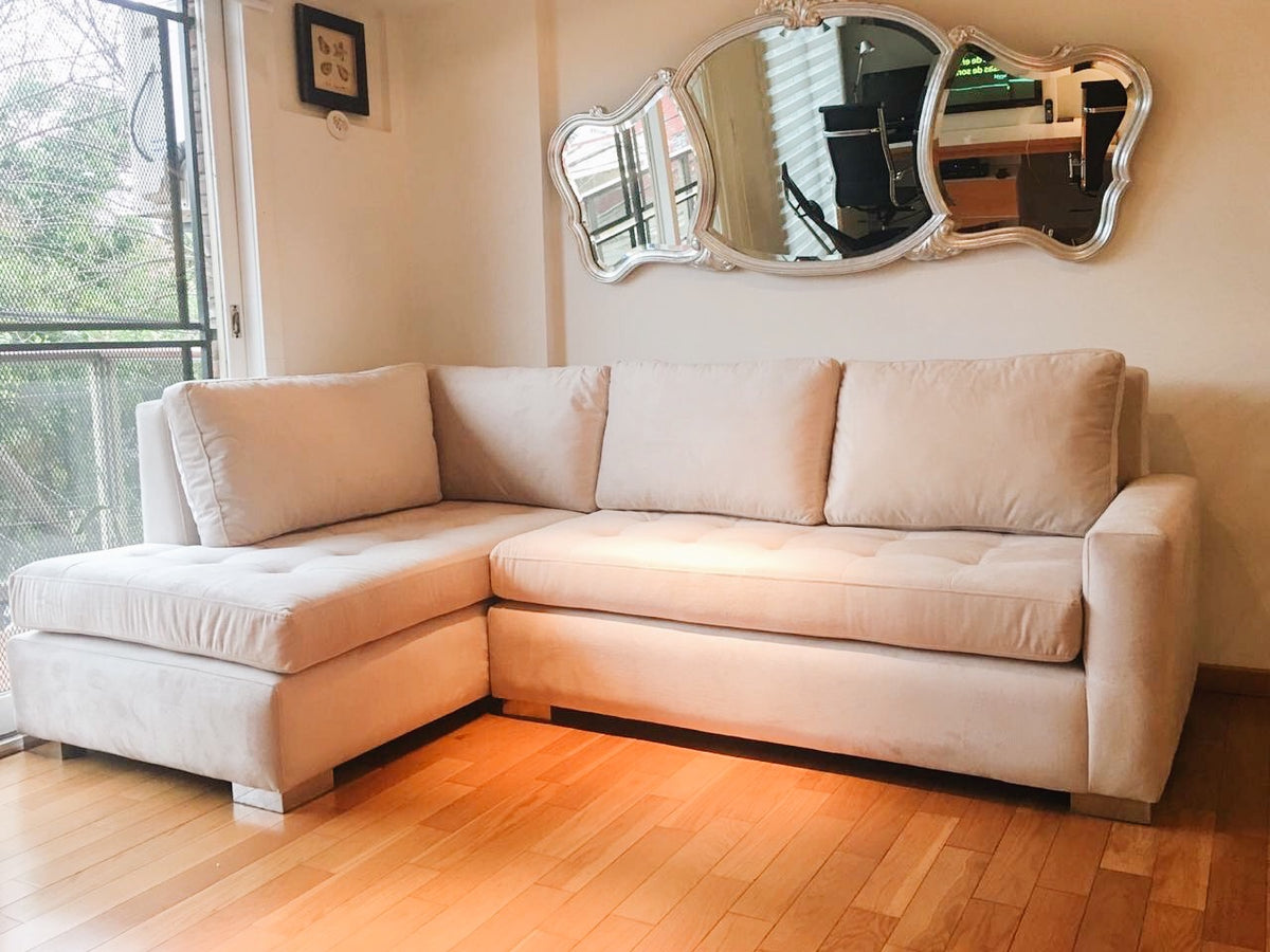 Esquinero crema con asiento capitoné y almohadones de respaldo sueltos, antes de sumar el puff, en el living de Nerina