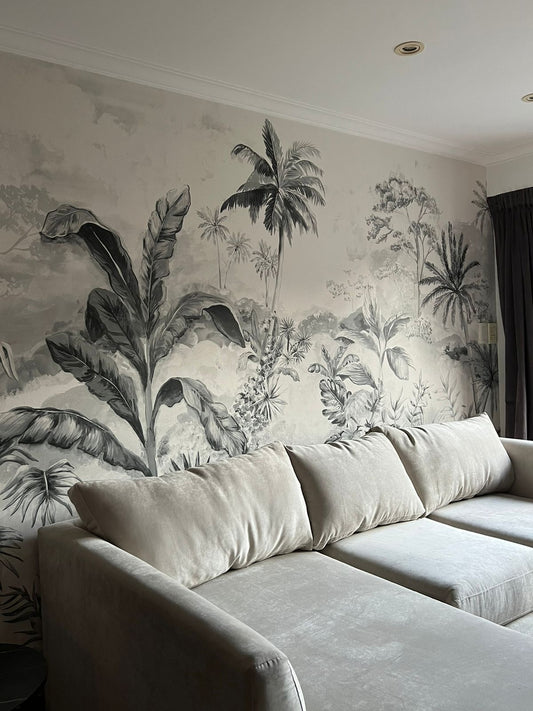 Esquinero Elton gris claro con almohadones de respaldo amplios frente a un empapelado tropical en blanco y negro con hojas y palmeras