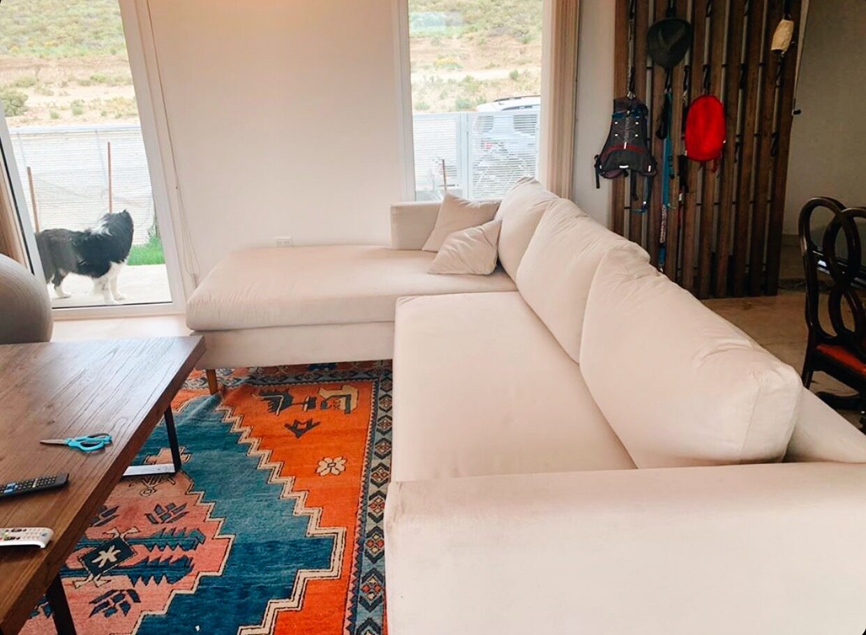 Sillón Esquinero Mirror blanco en living de casa de campo con alfombra kilim naranja y border collie, Argentina – Tienda de Banquitos
