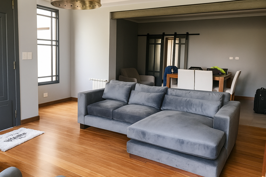 Sillón esquinero de tres cuerpos en tapizado gris, con cojines amplios y chaise longue, ubicado sobre piso de madera en un living moderno
